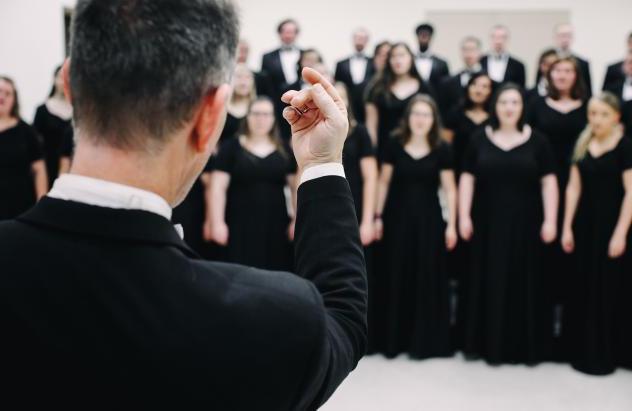 Concert Choir director conducts with the choir in the background out of focus